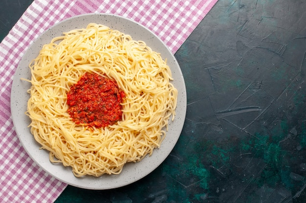 Vista superior de pasta italiana cocida con carne de tomate picada en la superficie azul oscuro