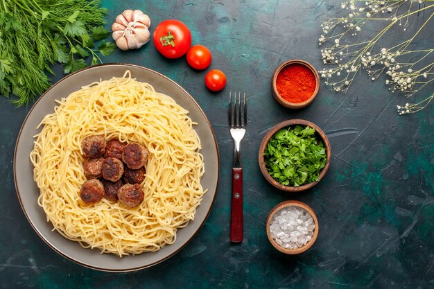 Vista superior de pasta italiana cocida con condimentos de albóndigas y verduras en la superficie azul oscuro