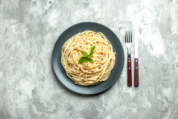 Vista superior de pasta italiana cocida con cubiertos sobre fondo blanco.