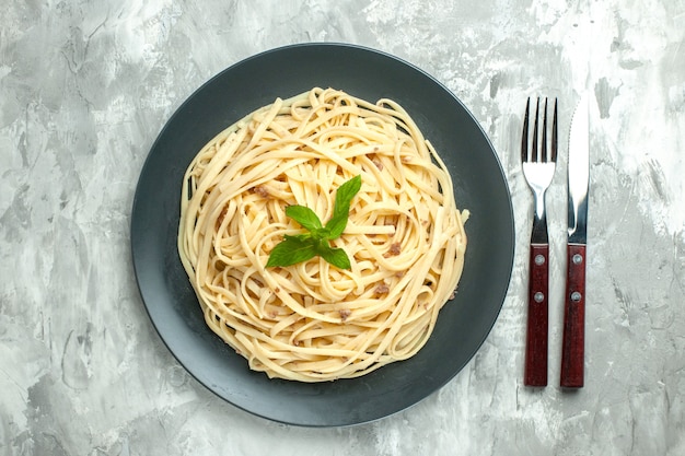 Vista superior de pasta italiana cocida con cubiertos sobre fondo blanco.