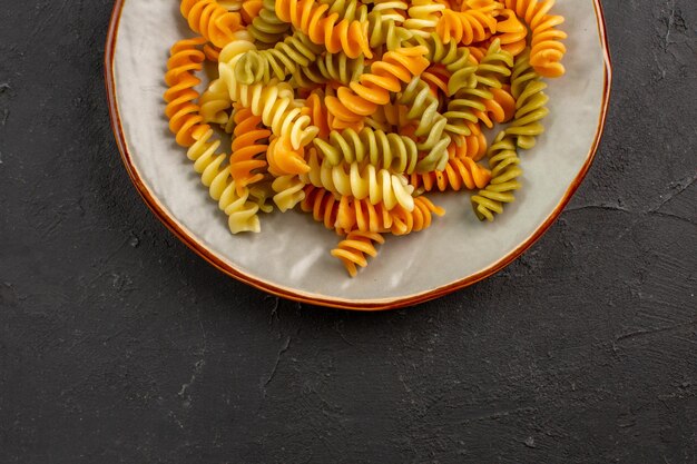 Vista superior de pasta italiana cocida inusual pasta en espiral dentro de la placa en el piso oscuro comida cocinando plato de pasta cena