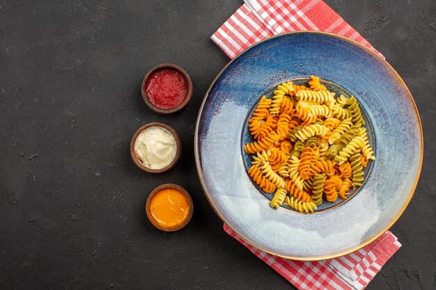Vista superior de pasta italiana cocida pasta espiral inusual dentro de la placa en el escritorio oscuro plato de cocción de pasta cena comida