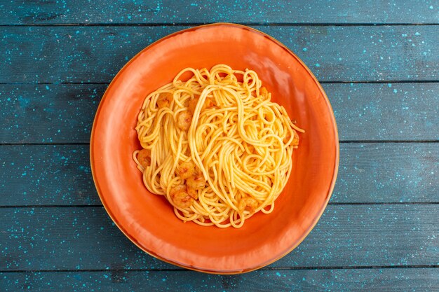 Vista superior de la pasta italiana cocida sabrosa dentro de la placa naranja sobre la superficie rústica de madera azul