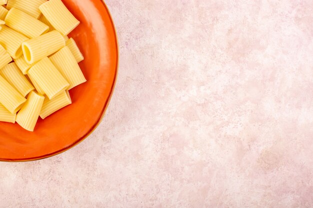 Una vista superior de la pasta italiana cocida sabrosa y salada dentro de la placa redonda naranja en el escritorio rosa