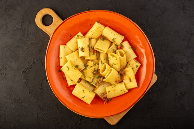 Una vista superior de la pasta italiana cocida sabrosa salada dentro de la placa redonda de naranja sobre el escritorio oscuro