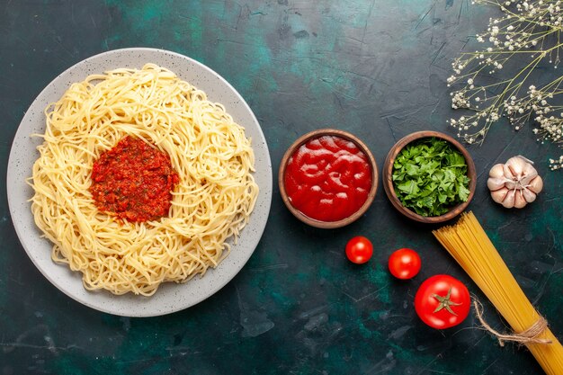 Vista superior de pasta italiana cocida con salsa de tomate de carne picada y condimentos en la superficie azul