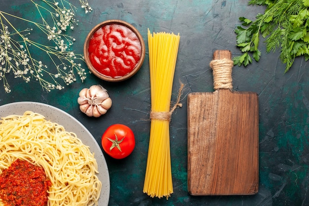 Vista superior de pasta italiana cocida con salsa de tomate carne picada en el escritorio azul