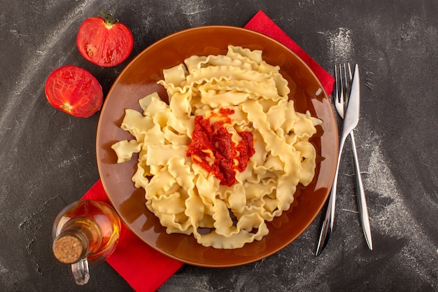 Una vista superior de pasta italiana cocida con salsa de tomate dentro de la placa con cubiertos y tomates