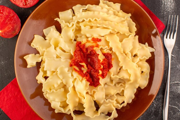 Una vista superior de pasta italiana cocida con salsa de tomate dentro de la placa con cubiertos y tomates