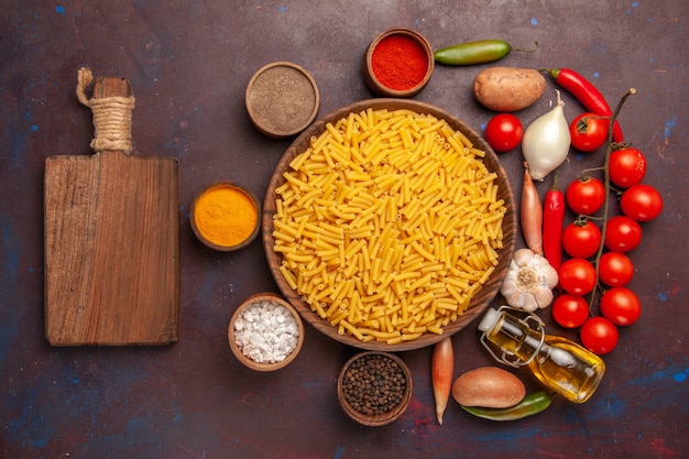 Vista superior de pasta italiana cruda con condimentos en la masa de comida de pasta de escritorio oscuro