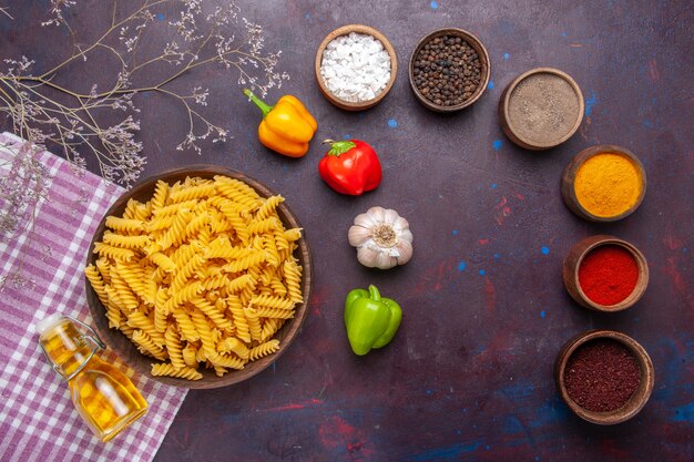 Vista superior de pasta italiana cruda con diferentes condimentos en el color de ingrediente de comida de pasta de superficie oscura