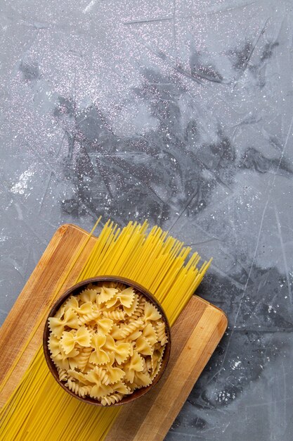 Una vista superior de pasta italiana cruda formada pequeña y larga dentro de la placa marrón en el escritorio gris pasta comida italiana foto