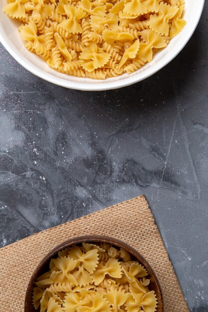 Una vista superior de pasta italiana cruda poco formada dentro de la placa marrón y blanca en el escritorio gris pasta comida italiana