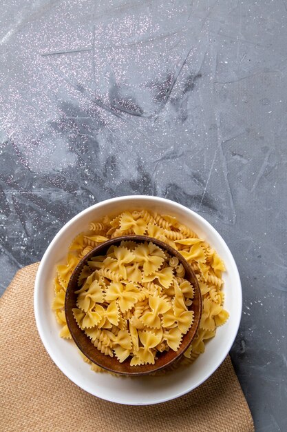 Una vista superior de pasta italiana cruda poco formada dentro de la placa marrón y blanca en el escritorio gris pasta comida italiana