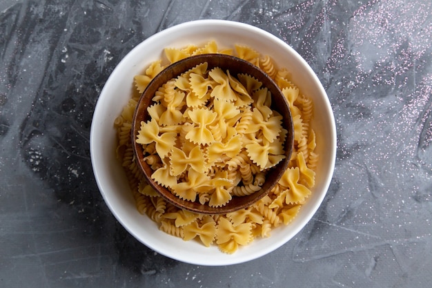 Una vista superior de pasta italiana cruda poco formada dentro de la placa marrón en el escritorio gris pasta comida italiana