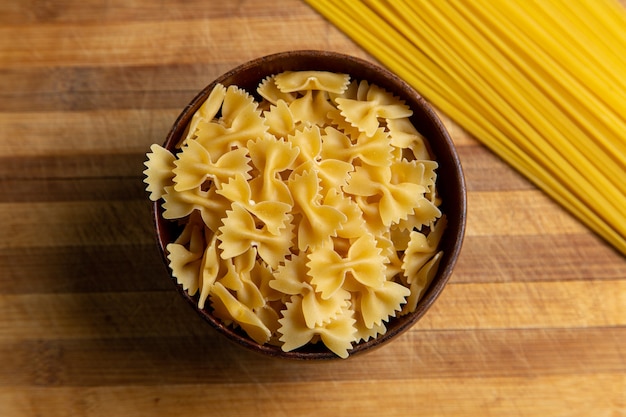 Una vista superior de pasta italiana cruda poco formada dentro de la placa marrón en el escritorio de madera pasta comida italiana