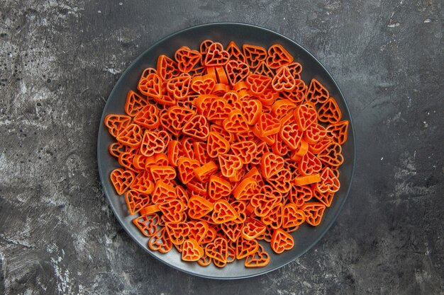 Vista superior de pasta italiana en forma de corazón en un plato negro sobre una mesa oscura