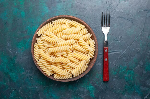 Vista superior de pasta italiana en forma de deliciosa pasta pequeña dentro de una olla marrón en el escritorio azul oscuro