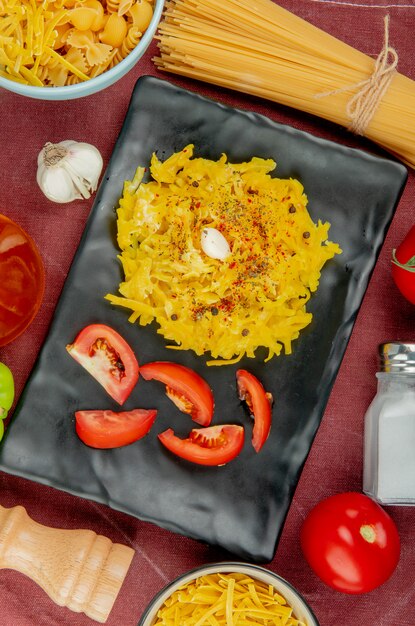 Vista superior de pasta de macarrones y tomate en rodajas en un plato con pasta diferente