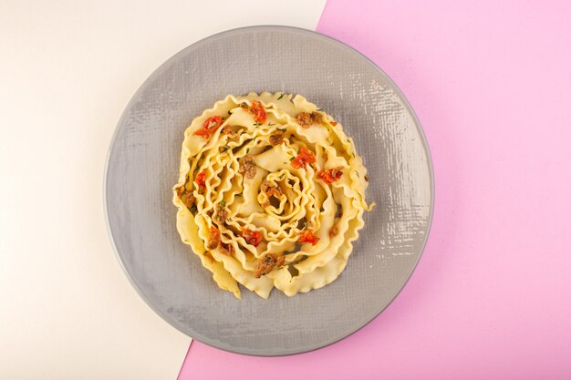 Una vista superior de pasta de masa con carne cocida y verduras dentro de la placa gris sobre blanco-rosa