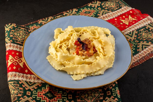 Una vista superior de la pasta de masa cocida sabrosa salada dentro de la placa azul redonda sobre alfombra diseñada y escritorio oscuro