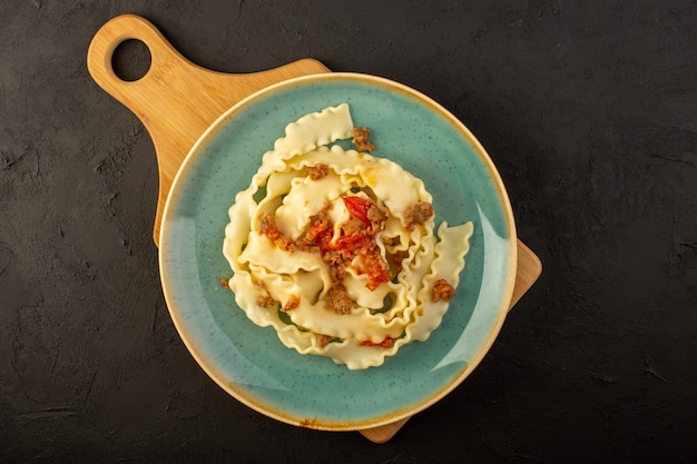 Una vista superior de la pasta de masa cocida sabrosa salada dentro de la placa verde redonda en el escritorio oscuro