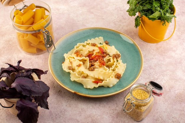 Foto gratuita una vista superior de la pasta de masa cocida sabrosa con verduras de carne y salada dentro de la placa verde redonda con flores y pasta cruda en el escritorio rosa