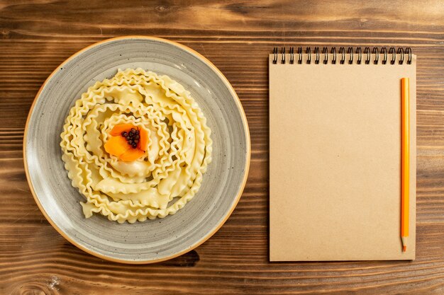 Vista superior de la pasta de masa cruda formada dentro de la placa en la mesa de madera marrón masa comida cruda pasta comida