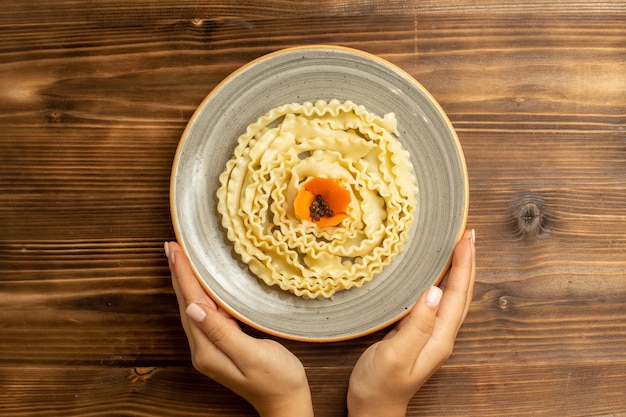 Vista superior de la pasta de masa cruda formada dentro de la placa en la mesa marrón masa de comida cruda comida de pasta