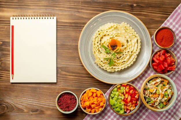 Vista superior de pasta de masa cruda con verduras y condimentos en la comida de pasta de comida de masa de mesa marrón