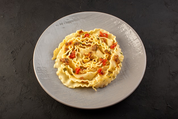 Una vista superior de pasta de masa con verduras en rodajas cocidas y carne dentro de la placa gris en la oscuridad