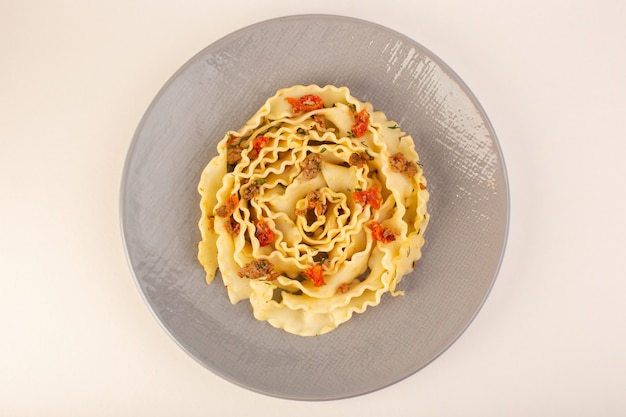 Una vista superior de pasta de masa con verduras en rodajas cocidas y carne dentro de la placa gris sobre blanco