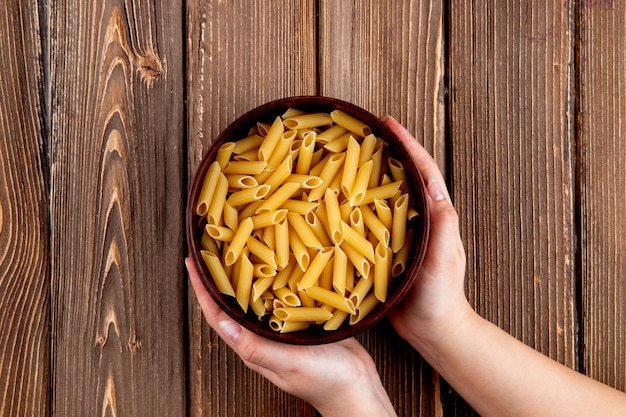 Vista superior de pasta penne en un tazón sobre fondo de madera