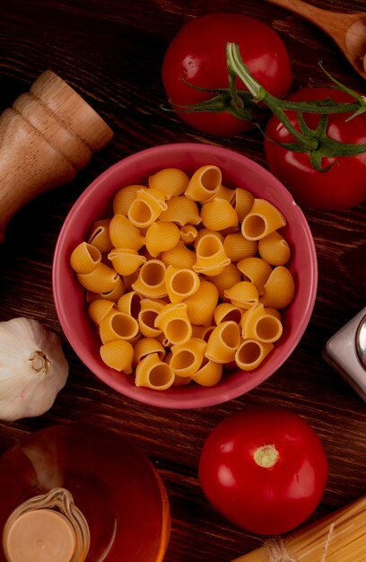 Vista superior de pasta pipe-rigate en un tazón con mantequilla de tomate salado sobre superficie de madera