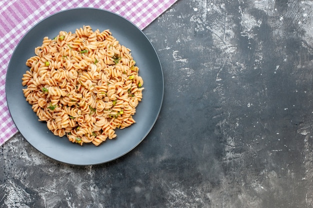 Vista superior de pasta rotini en plato redondo sobre mantel a cuadros blanco rosa sobre superficie oscura con espacio de copia