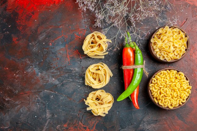 Vista superior de pastas crudas pimientos de cayena en diferentes colores y tamaños atados entre sí con una cuerda en la mesa de colores mezclados