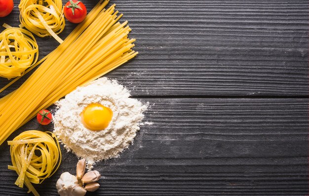 Vista superior de las pastas crudas de los tallarines y de los espaguetis con los ingredientes en tablón de madera