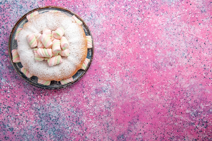 Foto gratuito vista superior de un pastel de azúcar en polvo con malvaviscos dulces en superficie rosada