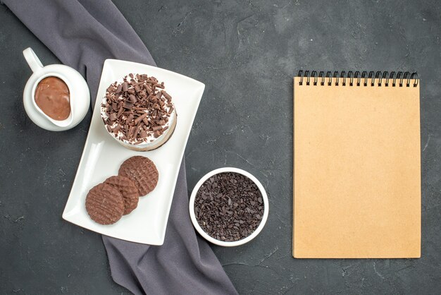 Vista superior de pastel de chocolate y galletas en tazones de fuente rectangular blanca con chocolate sobre fondo oscuro aislado