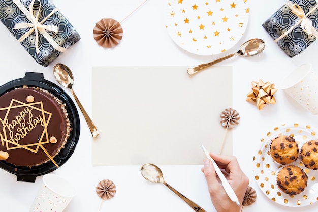 Vista superior pastel de cumpleaños y galletas con invitación de cumpleaños vacía