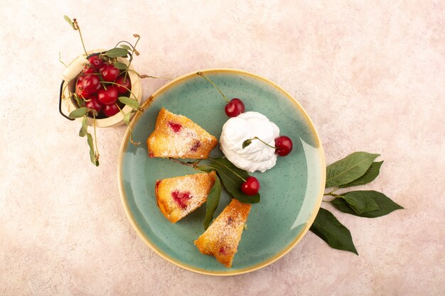 Una vista superior pastel de frutas al horno delicioso en rodajas con cerezas rojas en el interior y azúcar en polvo dentro de la placa redonda verde en rosa