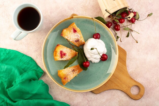Una vista superior pastel de frutas al horno delicioso en rodajas con cerezas rojas en el interior y azúcar en polvo dentro de la placa verde redonda con té en rosa