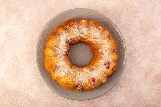 Una vista superior de pastel de frutas horneado delicioso redondo con frutos rojos en el interior y azúcar en polvo dentro del plato redondo en rosa