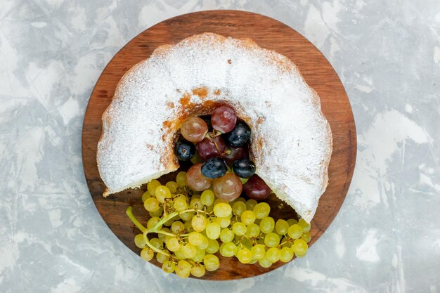 Vista superior pastel en polvo delicioso pastel horneado con uvas frescas sobre superficie blanca
