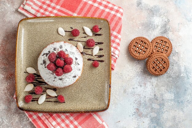 Vista superior del pastel recién horneado con frambuesas y galletas en el cuadro blanco