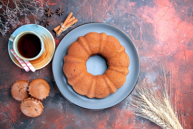 Vista superior de un pastel, una taza de té, plato azul de pastelitos, magdalenas, canela, anís estrellado, espigas de trigo