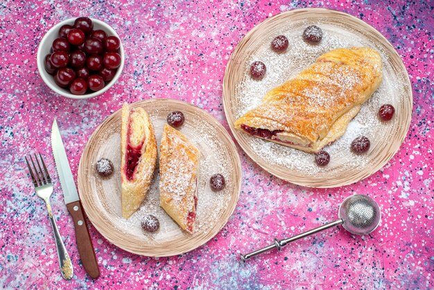 Vista superior de pastelería de cereza deliciosa y dulce en rodajas con guindas frescas dentro de las placas en el escritorio de color pastel galleta azúcar dulce hornear
