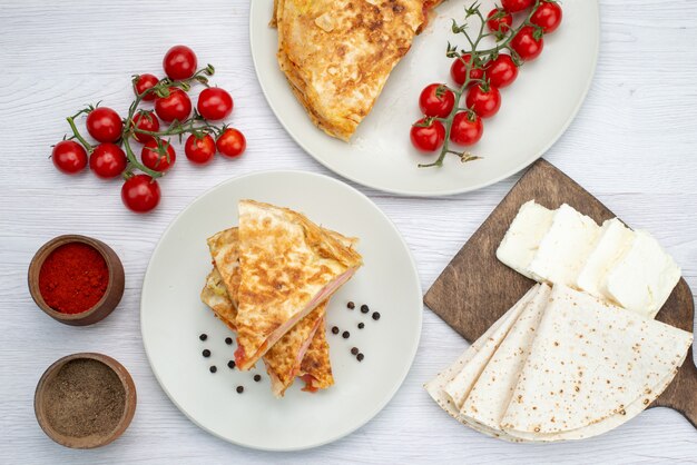 Vista superior de pastelería con verduras junto con condimentos de queso blanco y tomates frescos en el almuerzo de comida de fondo blanco