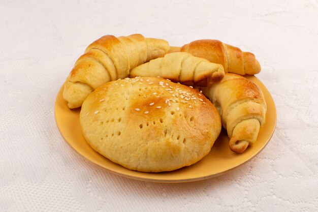 Vista superior de pasteles y croissants dentro de la placa naranja en el piso blanco