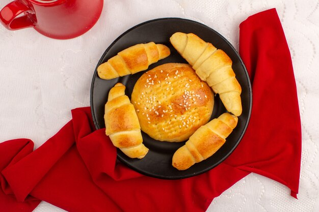 Vista superior pasteles croissants dentro de la placa negra en el tejido rojo en el piso blanco